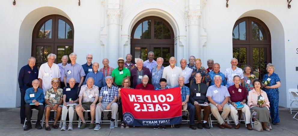 several dozen older alumni hold a Golden Gaels flag